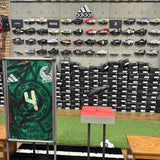 Display of sports shoes and accessories in a store with a green and black patterned shoe on a stand.